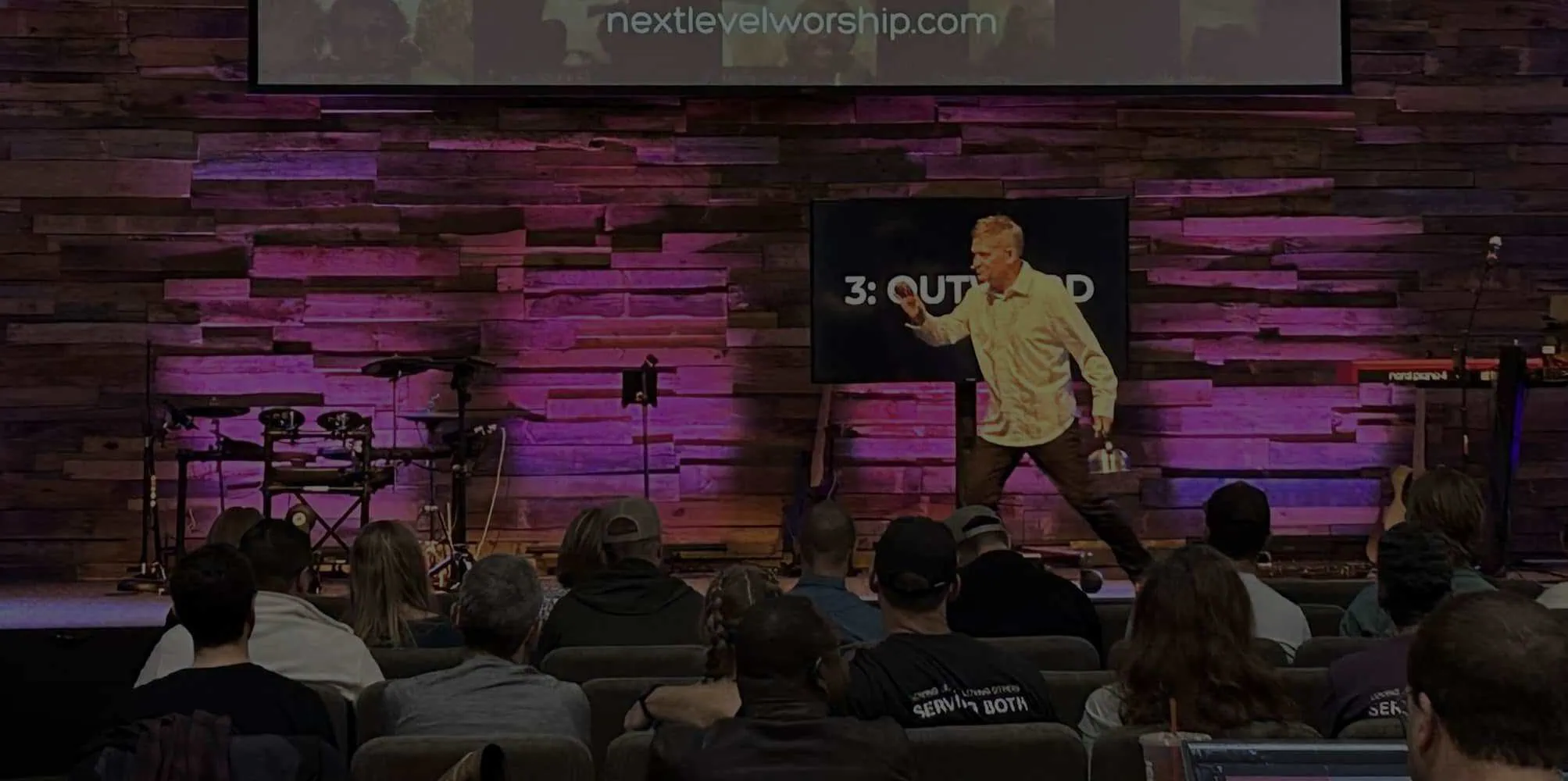 Speaker presenting at NLW International worship conference with audience.