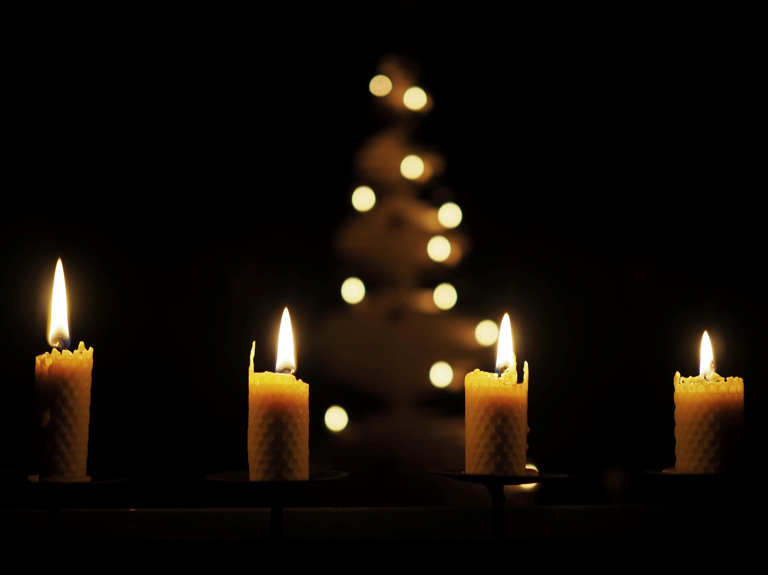 Candlelit worship candles with a blurred Christmas tree in the background, symbolizing faith and cel.