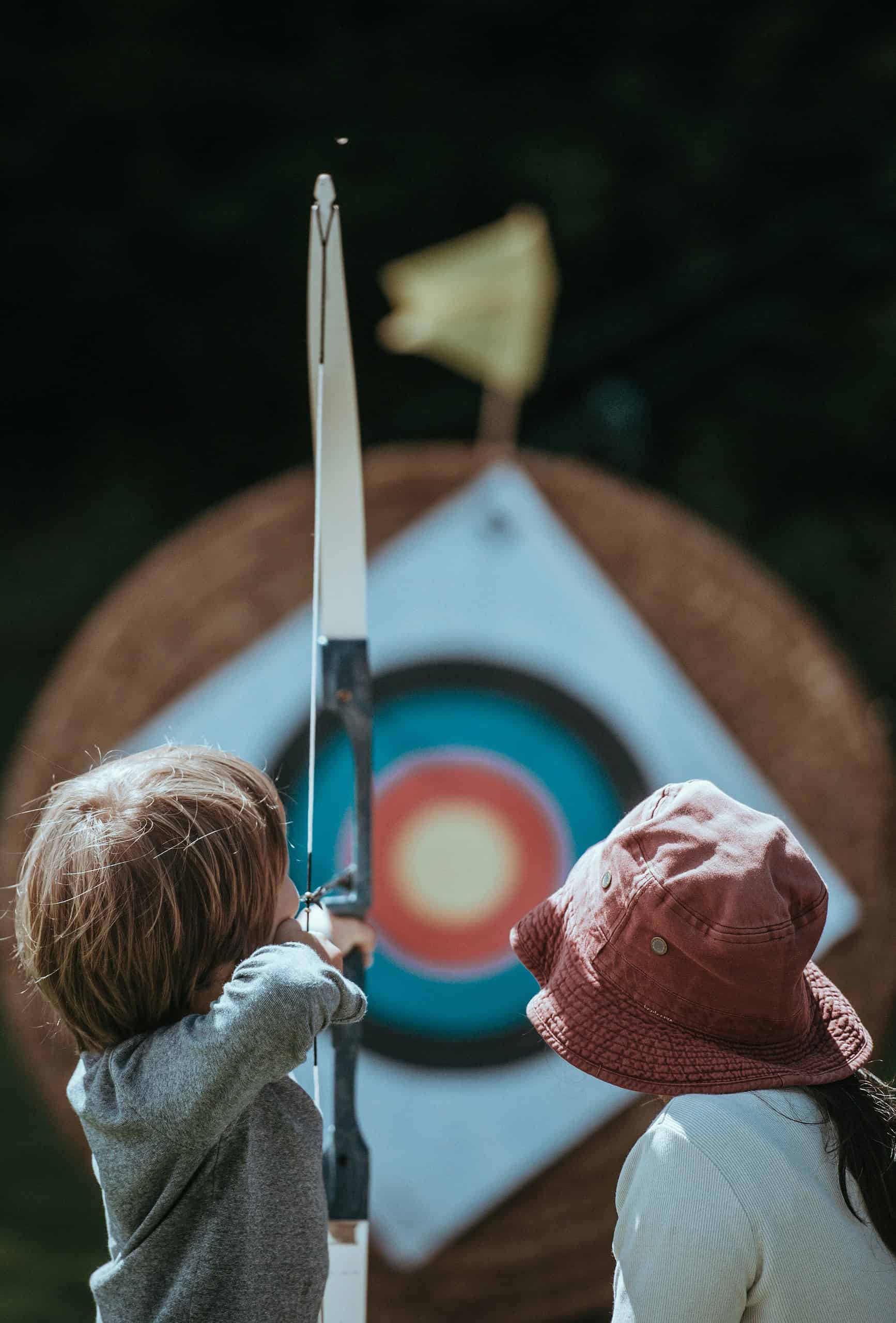 Children practicing archery outdoors with a target in the background.