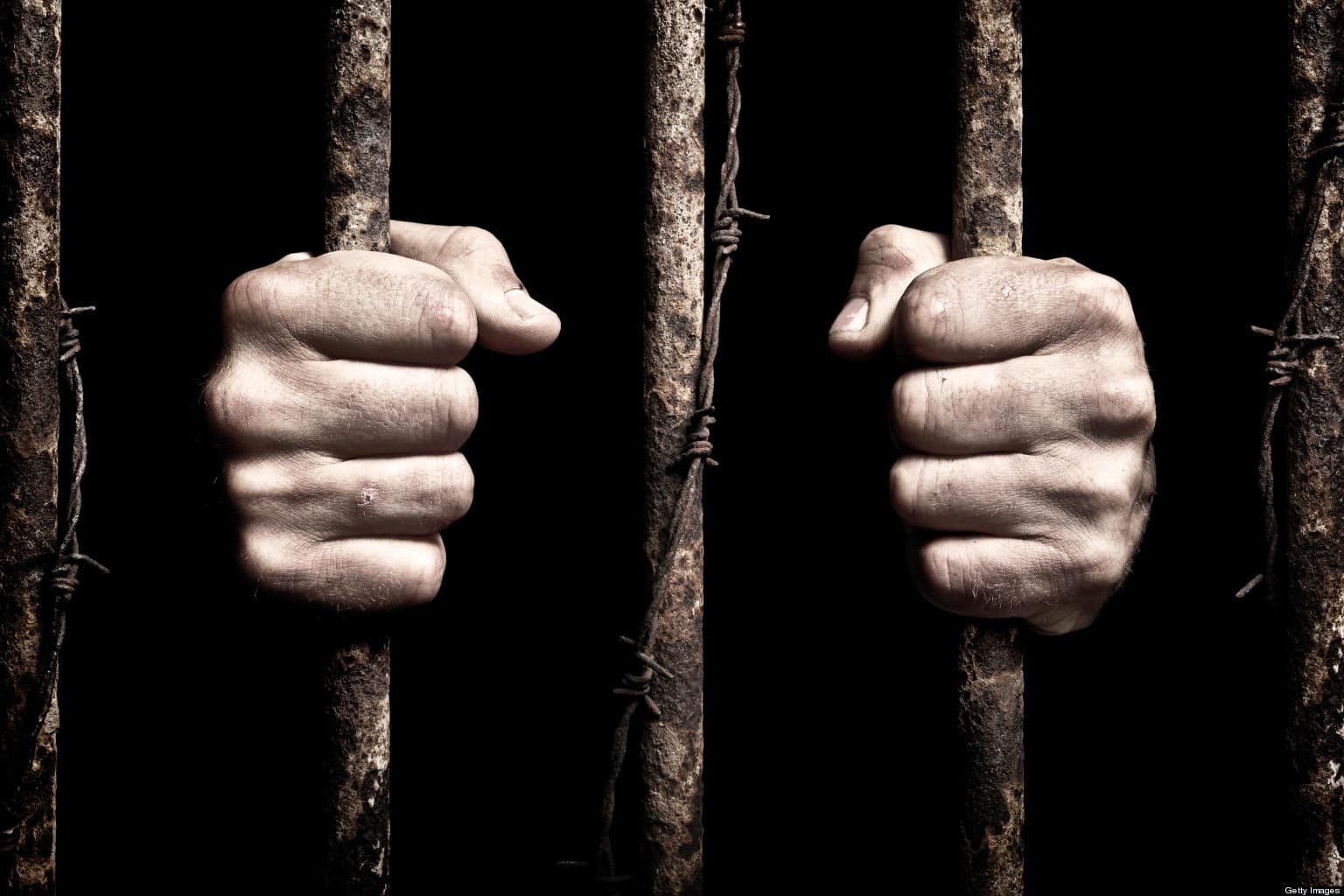 Prisoner hands gripping metal bars, symbolizing confinement and faith in overcoming challenges.