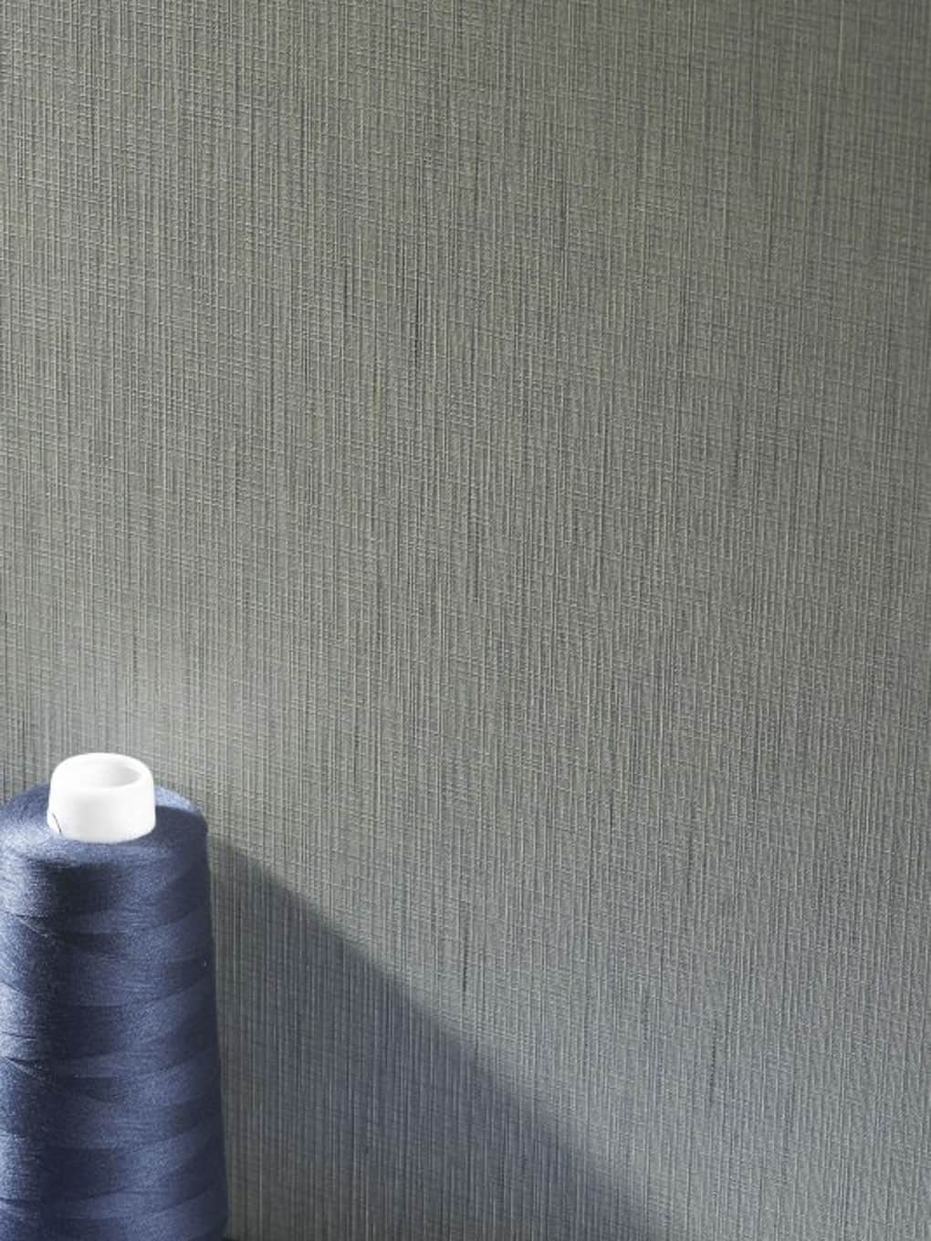 Gray textured wall background with a spool of navy blue sewing thread in the corner.