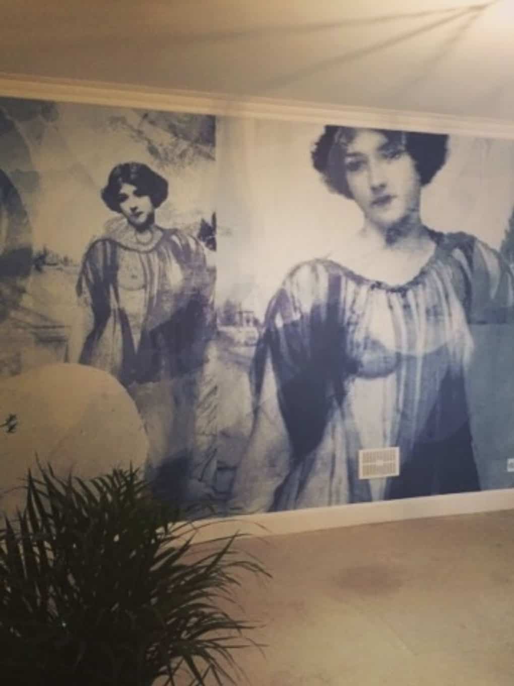 Vintage black and white mural of two women in historical attire on gallery wall.