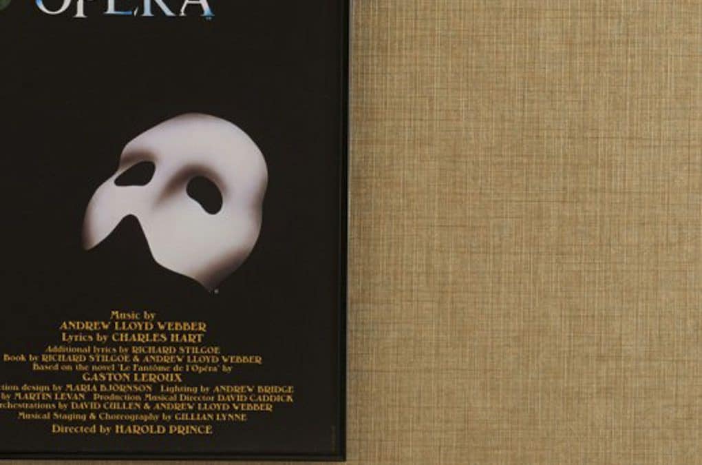 The Phantom of the Opera playbill with a white mask and red rose, displayed on a beige textured back.