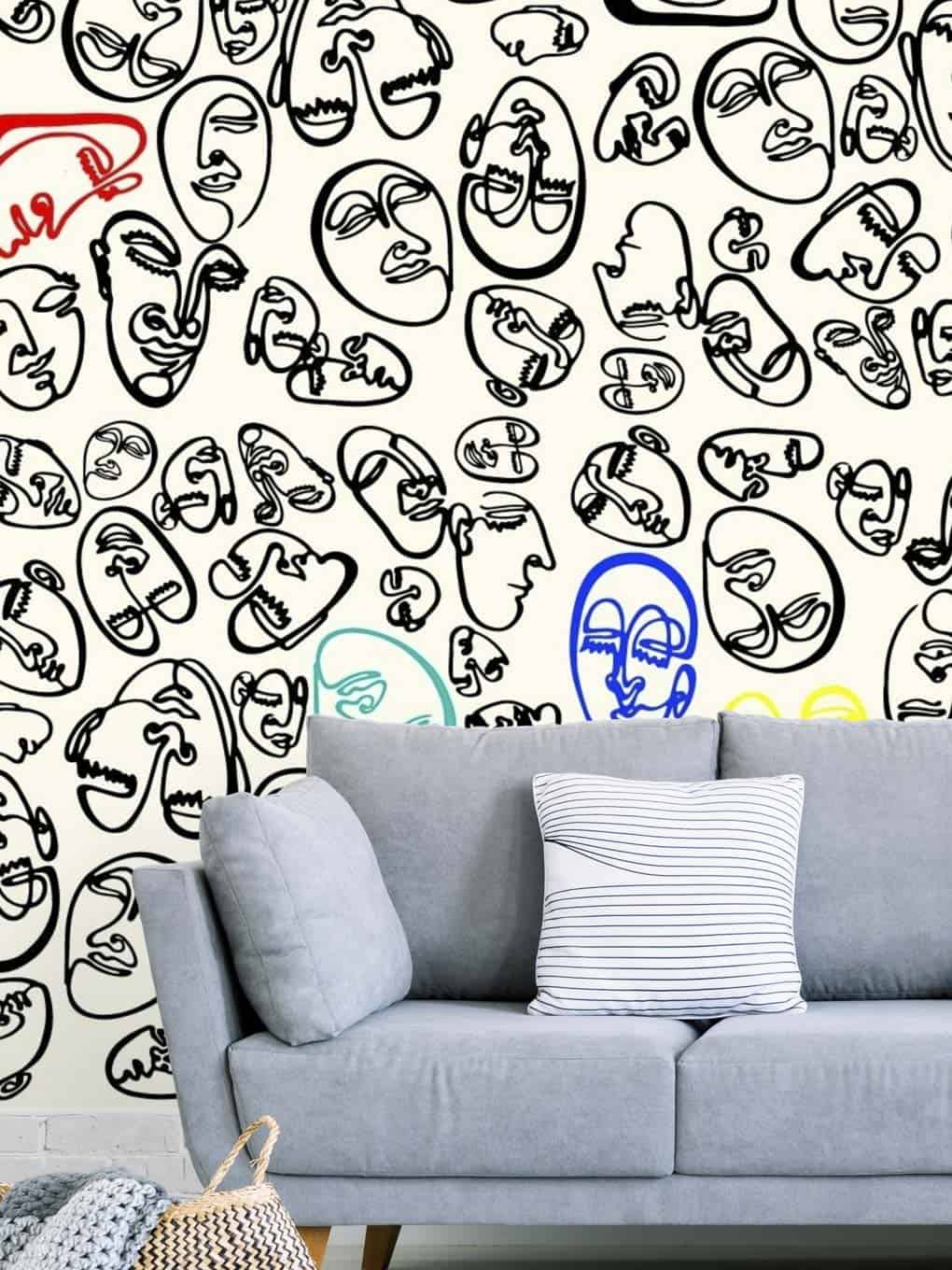 Abstract line art faces wall mural behind a modern gray sofa with a striped cushion.