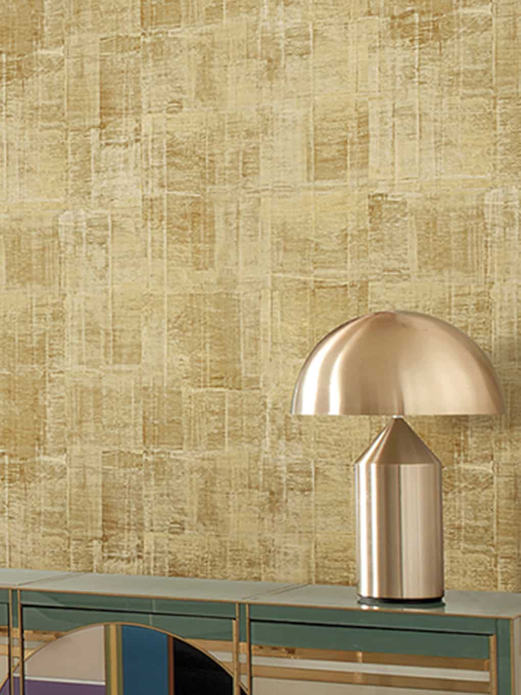 Gold table lamp with a sleek, modern design on a green sideboard, set against a textured beige wall.