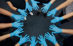 Many hands in blue nitrile gloves together in a circle.