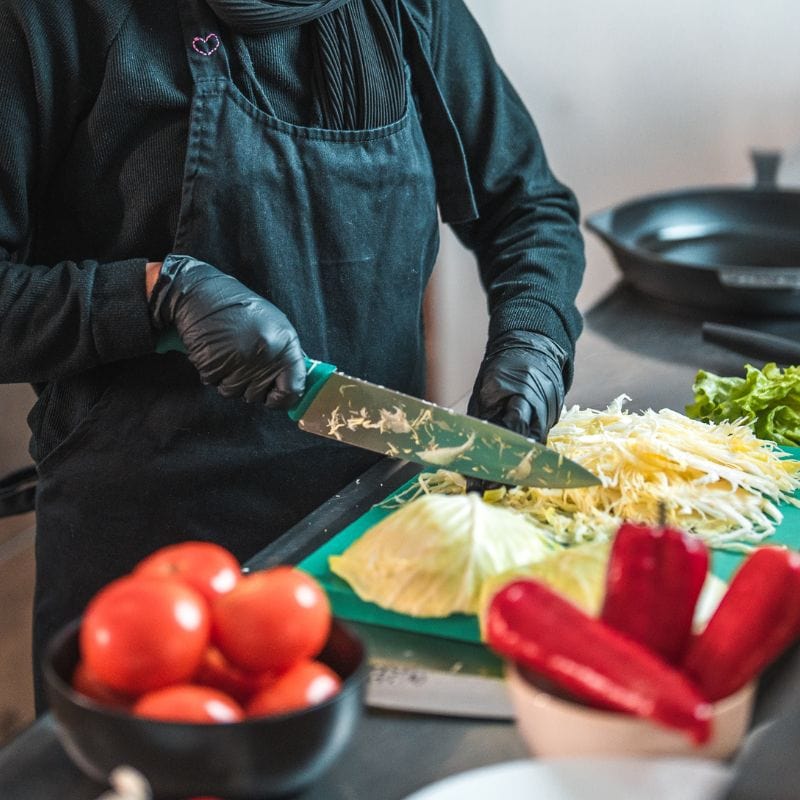 Chef wearing nitrile gloves prepares vegetables using a knife. Food safety.