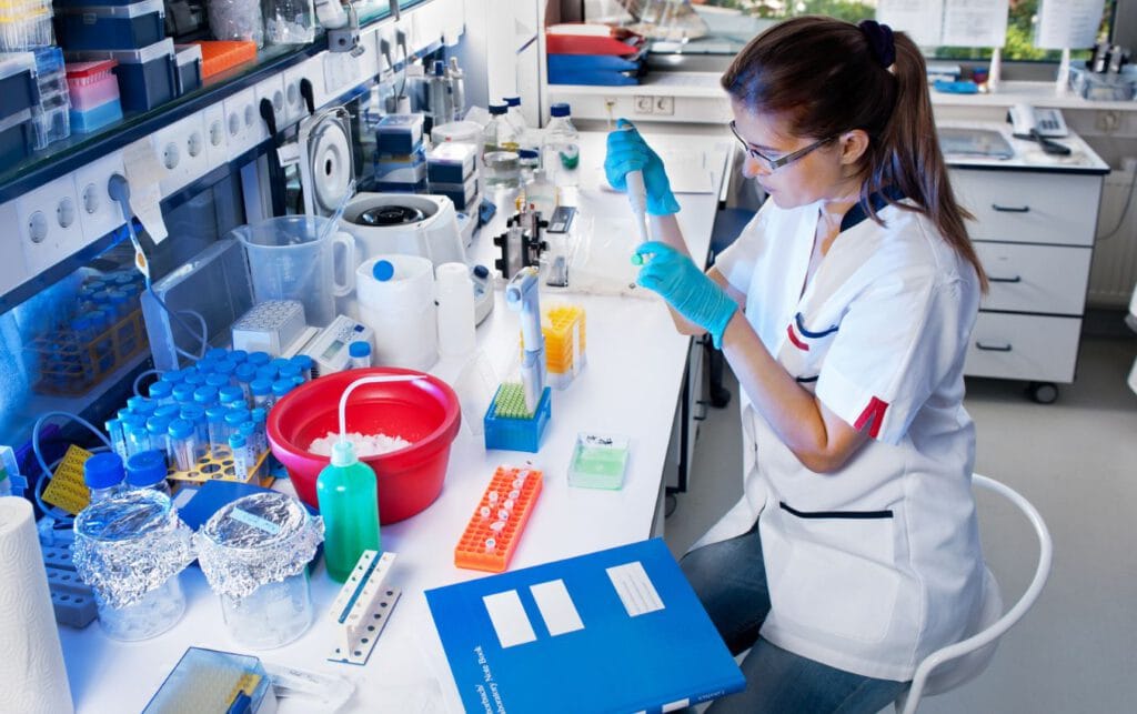 Scientist wearing gloves performs lab work, using pipettes and test tubes.