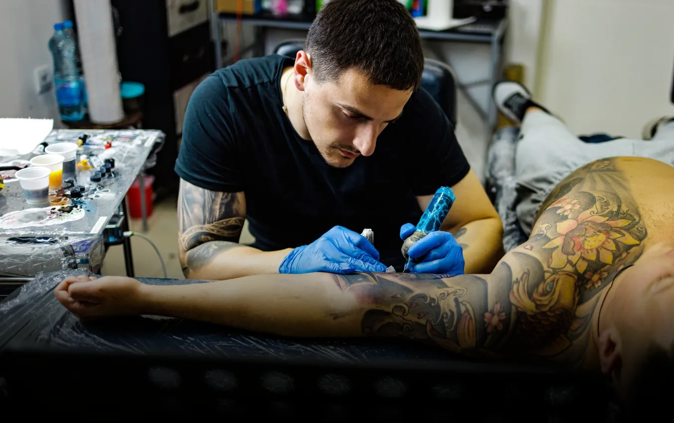 Tattoo artist wearing nitrile gloves carefully applies ink to a client's arm.