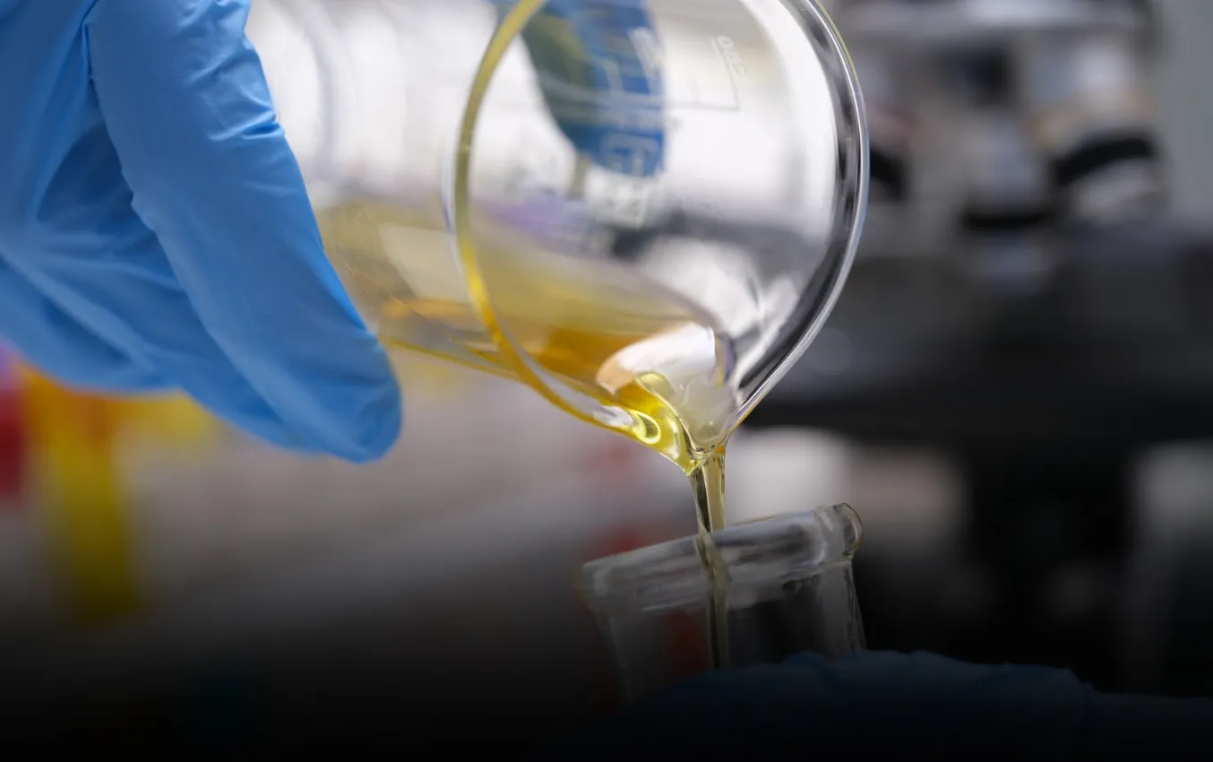 Gloved hand pouring yellow liquid, testing nitrile glove oil resistance.