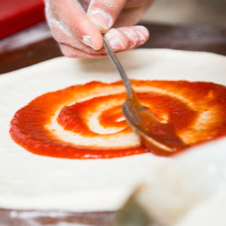 Master the Art of Pizza: Simple Steps to Perfect Easy Pizza Dough | The Not so Modern Housewife spreading sauce on pizza crust with a spoon - easy pizza dough