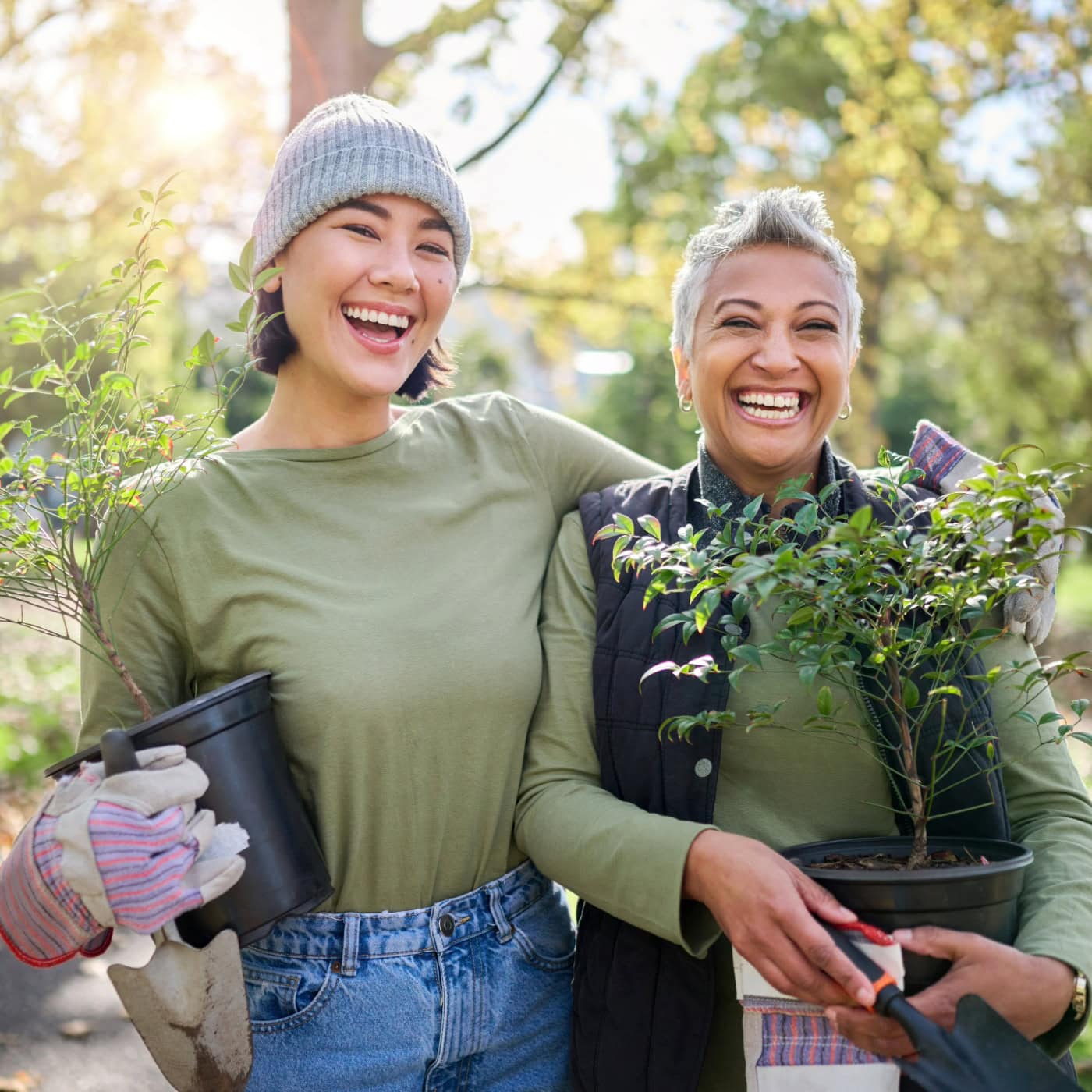 Florida Summer Planting Guide: 7 Smart Crops That Thrive in the Heat | The Not so Modern Housewife Two smiling women holding potted plants and gardening tools, highlighting the community and joy found in shared gardening experiences from the Florida Summer Planting Guide.
