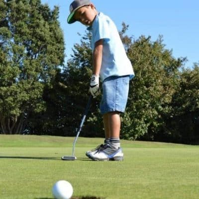 Boy playing golf on a green in New Plymouth, New Zealand.