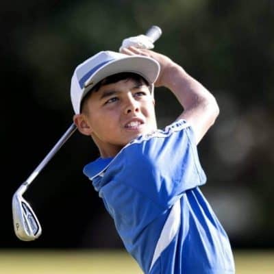 Young boy playing golf, practicing swing outdoors at a golf course.