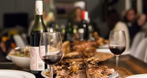 Showing a rustic dinner table with slow cooker lamb, red wine and plates ready to serve.