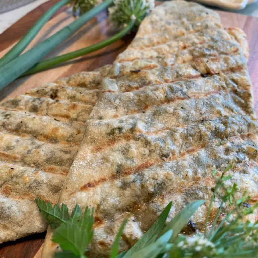 Softened butter being brushed over a hot, freshly cooked Jingalov Hat directly on the griddle, melting into the blistered surface.