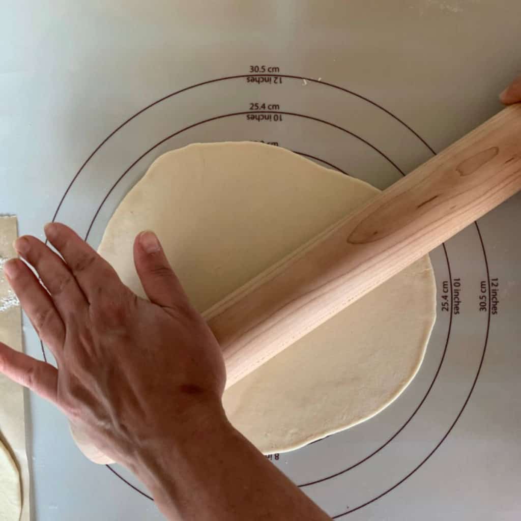 A thin circle of Armenian flatbread dough rolled out to 8 inches, sitting on a lightly floured wooden surface, ready to be filled.