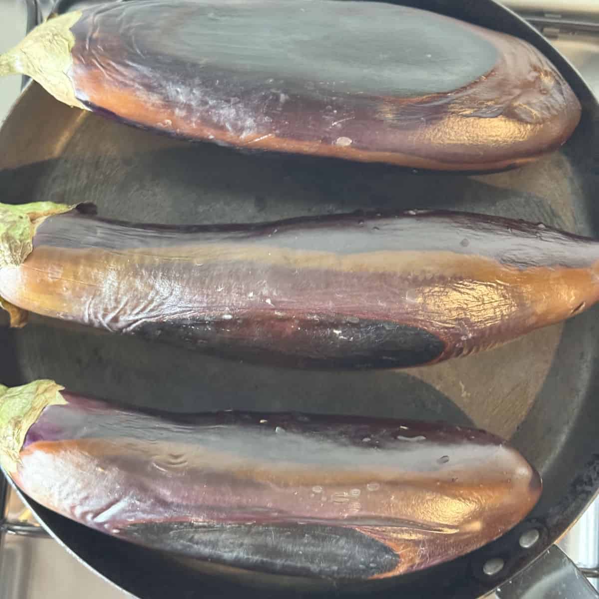 Roasting eggplants on a blue steel pan.