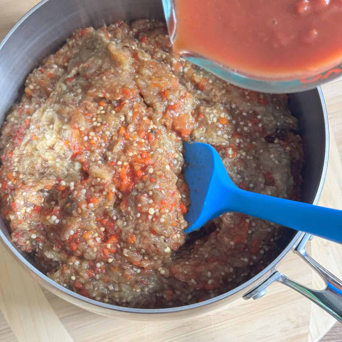 Adding the diluted tomato paste to the roasted vegetable puree.