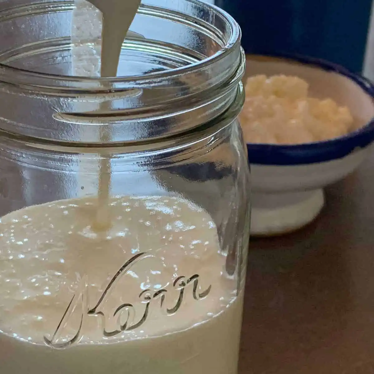 pouring kefir into a glass jar.