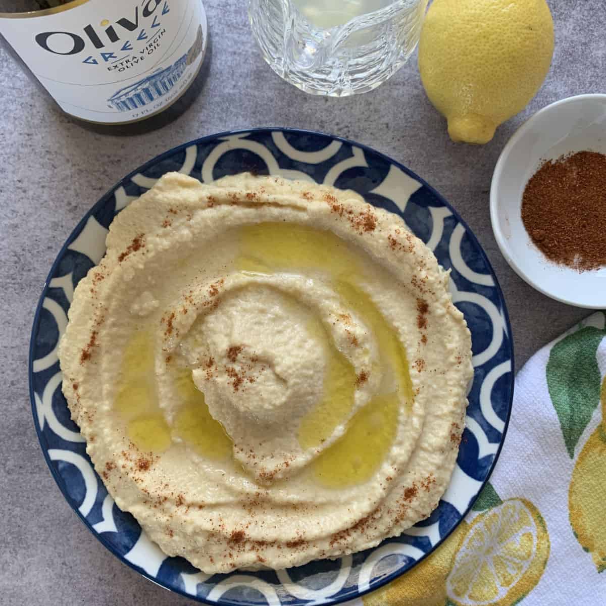 Hummus on a plate with olive oil, lemon and paprika next to it.