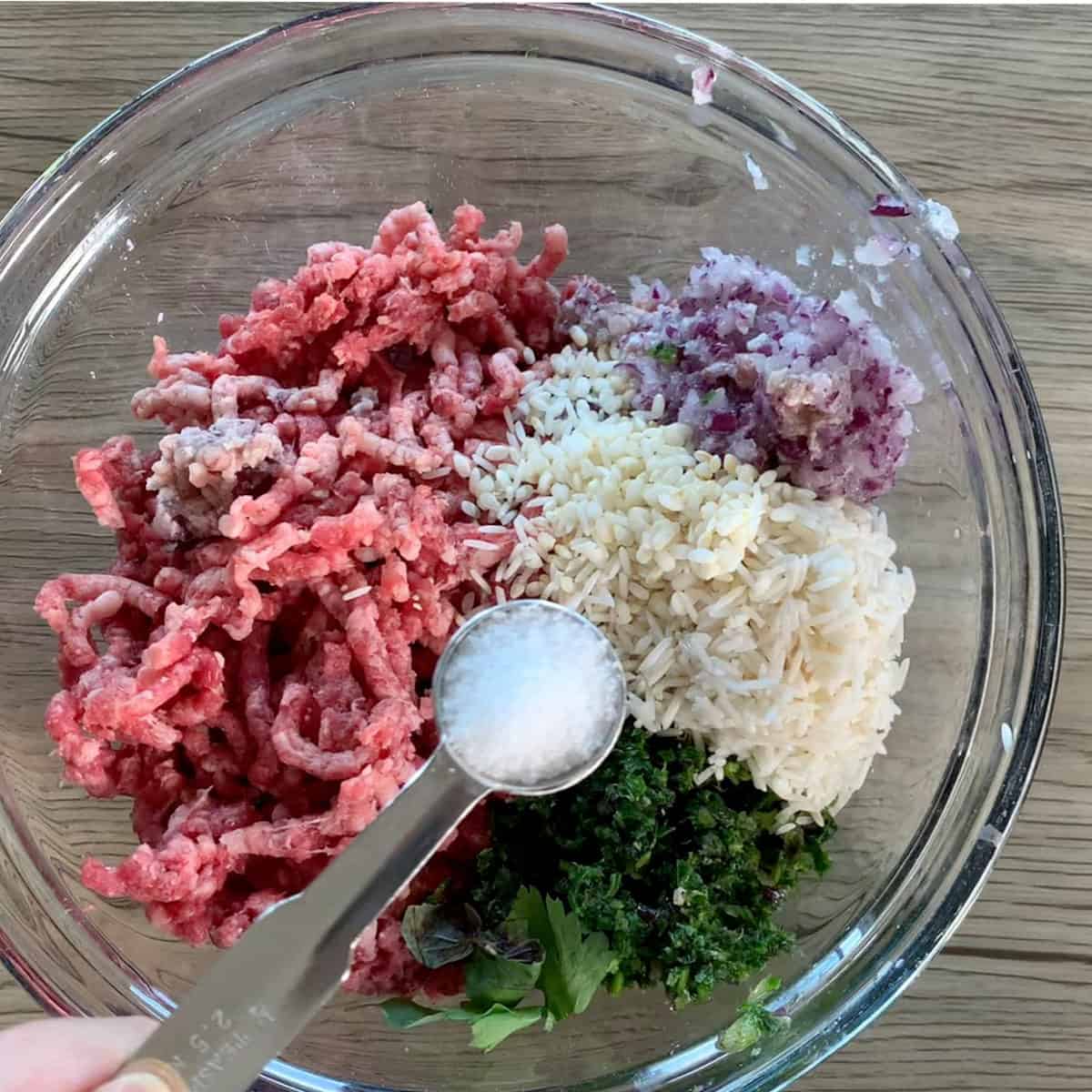Adding salt to ground beef, onions, herbs, rice mixture.