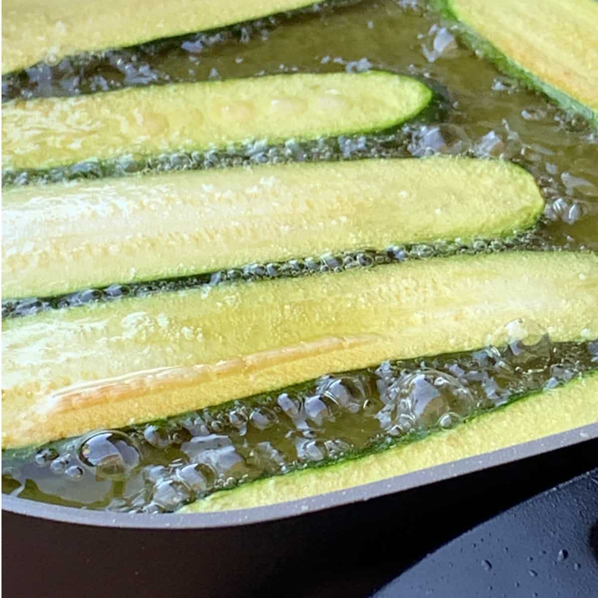 Zucchini slices are frying in a oil.
