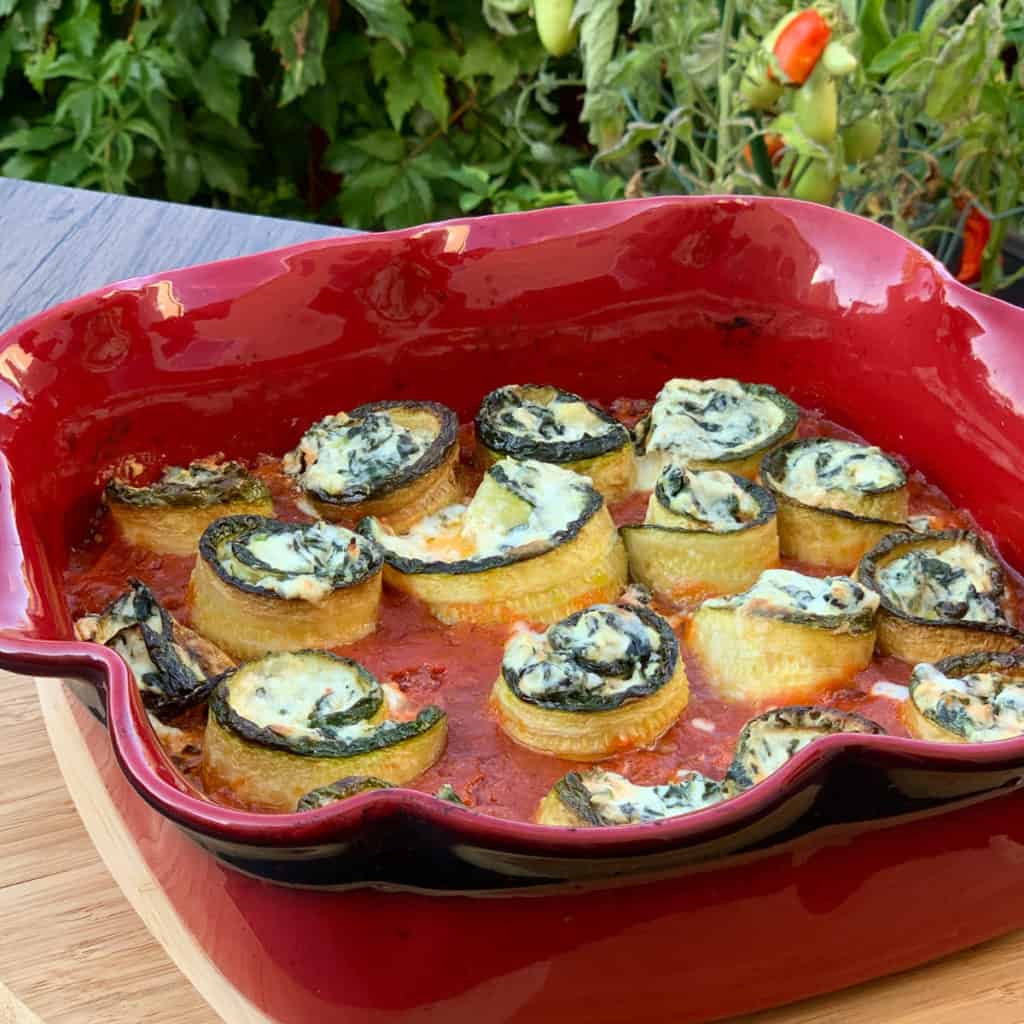 Zucchini roll ups in a red clay dish.