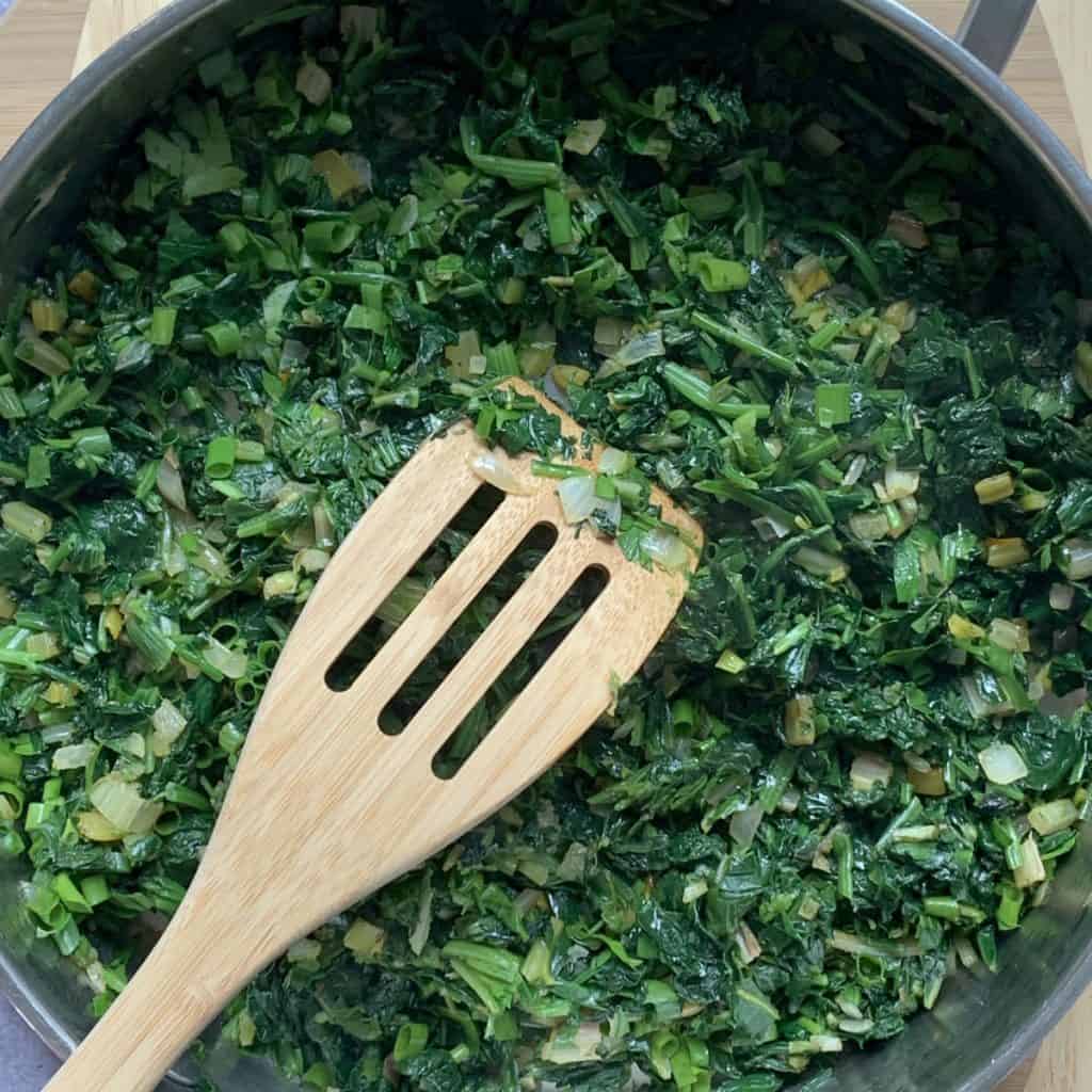 The spinach mixture in a saute pan with a wooden spoon.