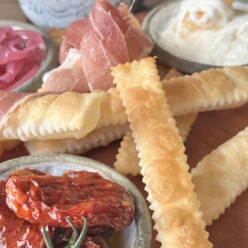 Gnocco Fritto on a wooden board with sun dried tomatoes,stracciatella cheese, and prosciutto.