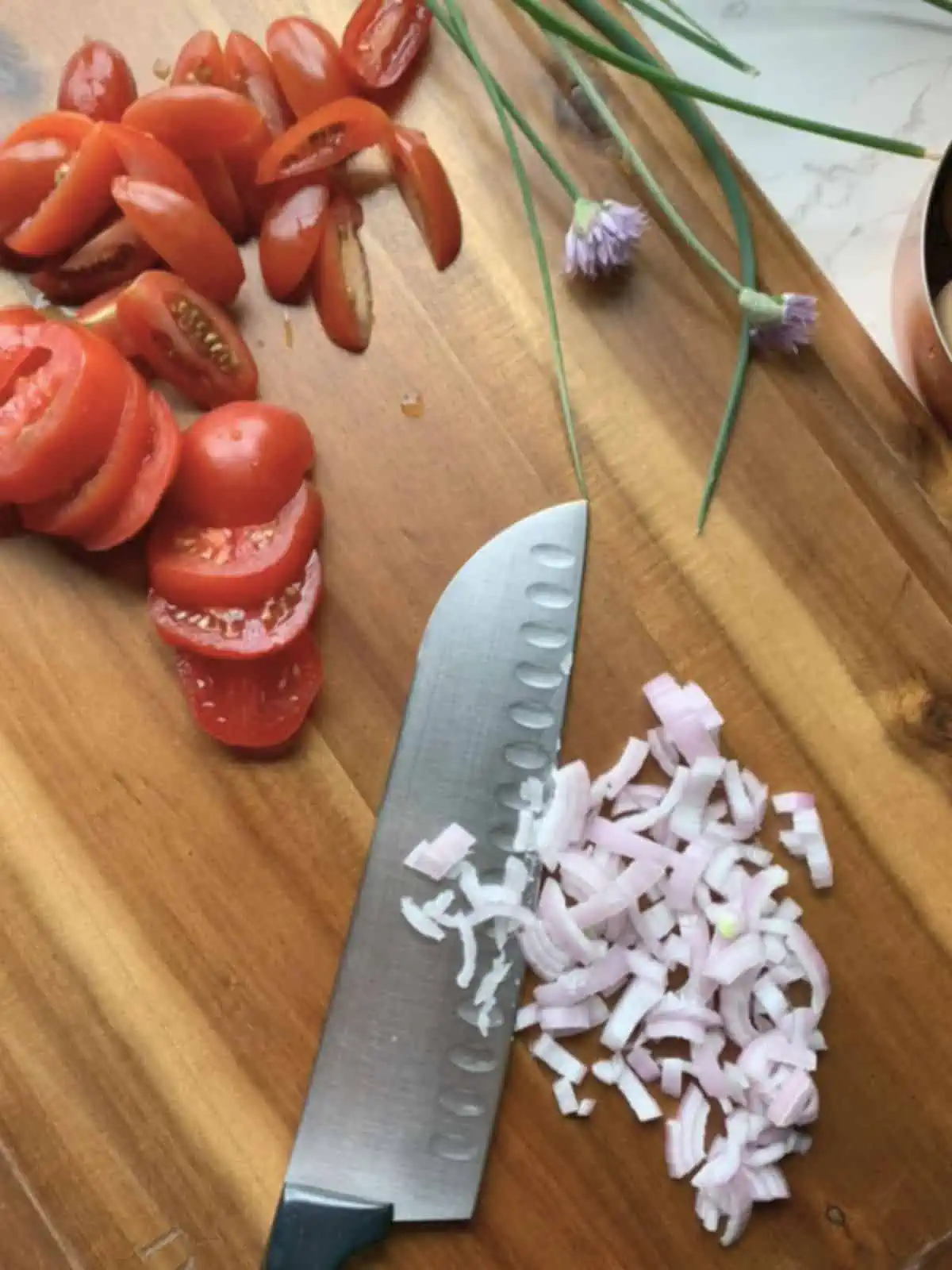 Chopped shallots and tomatoes on a cutting board. 