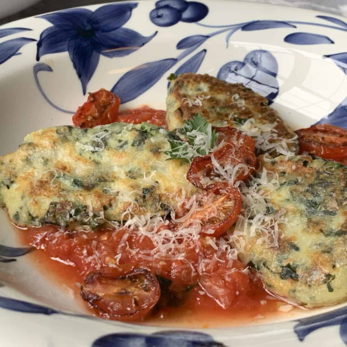 Ricotta kale gnudi in a plate with tomatoes.