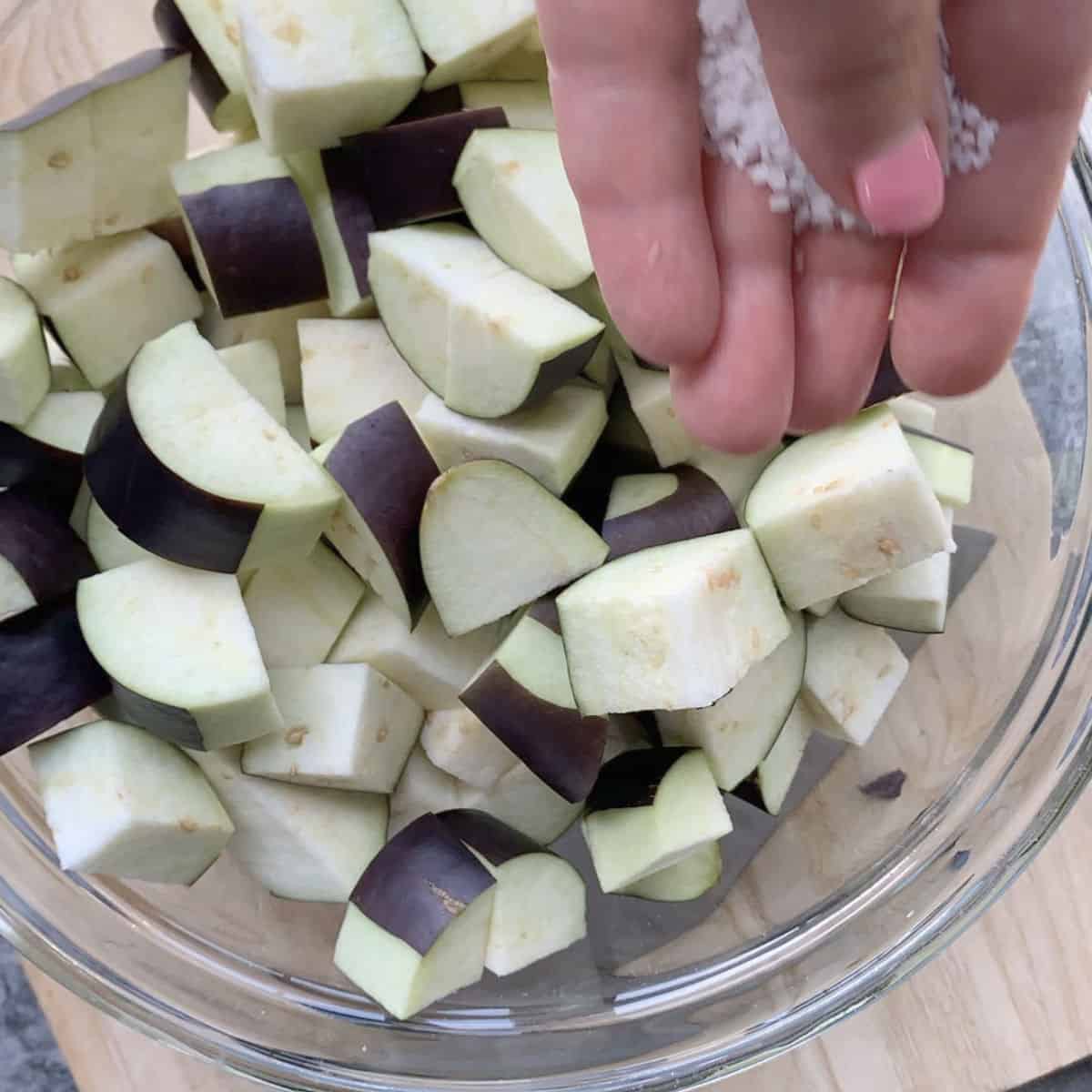 Sprinkling salt on a peeled and cubed eggplants.
