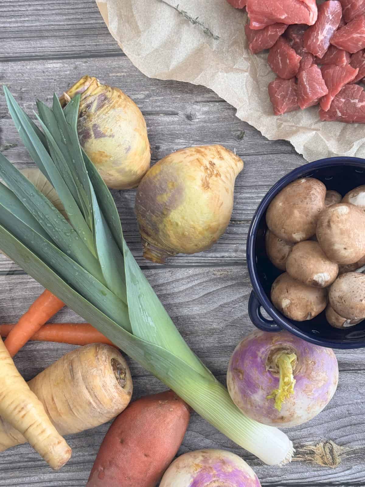 Root vegetables, leeks, and stew meat on a wooden board.