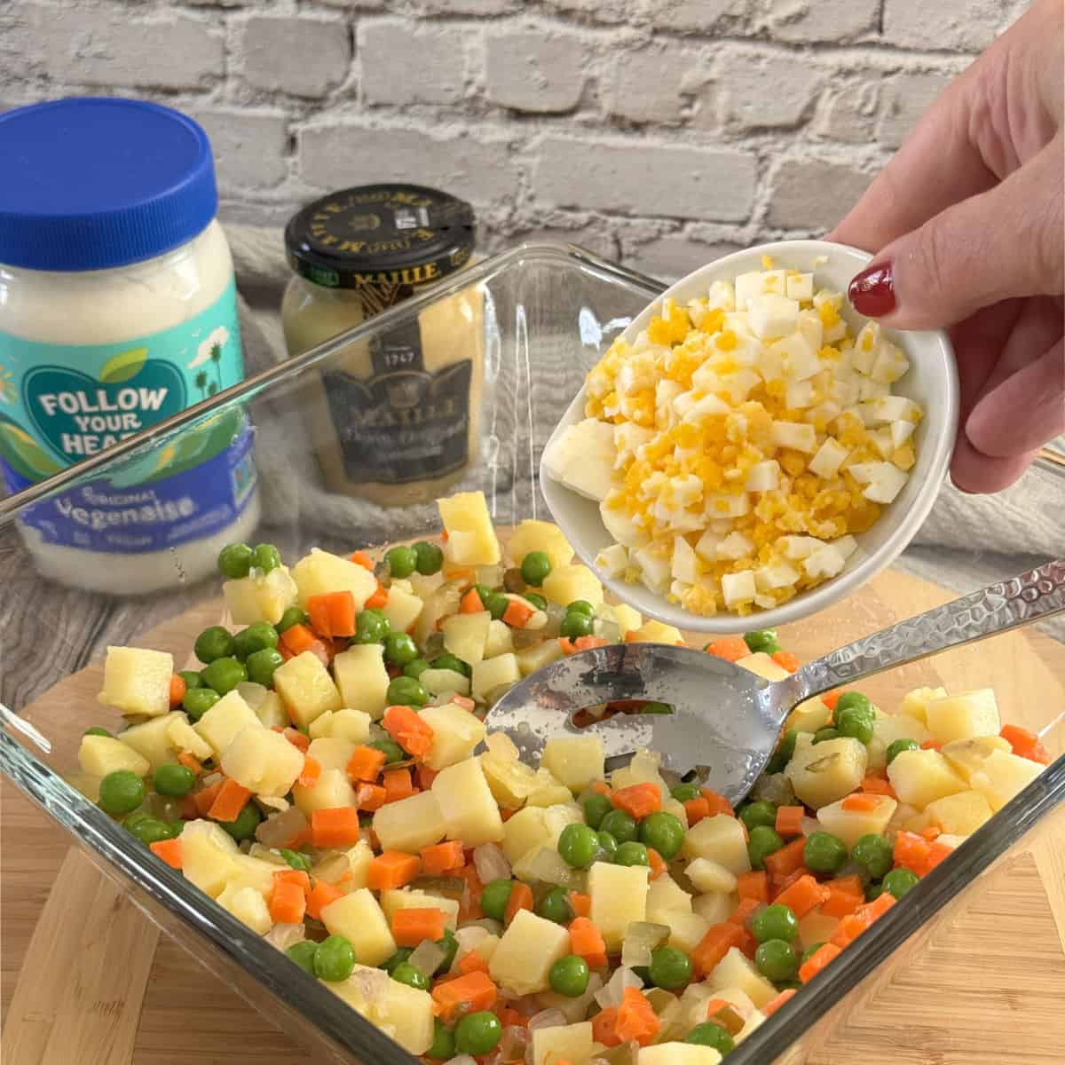Adding chopped eggs to the olivier salad.