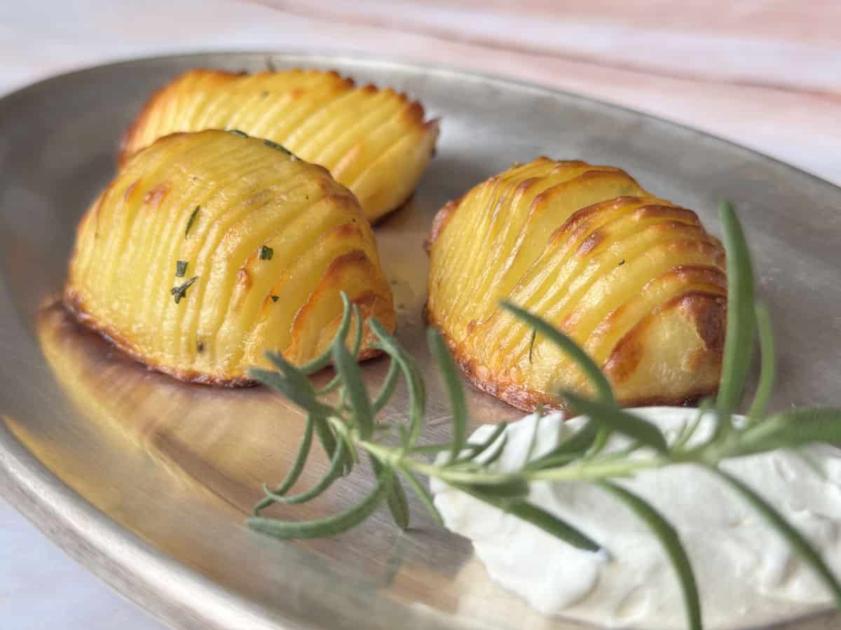 Hasselback potatoes on a silver plate with a dollop of sour cream and rosemary.