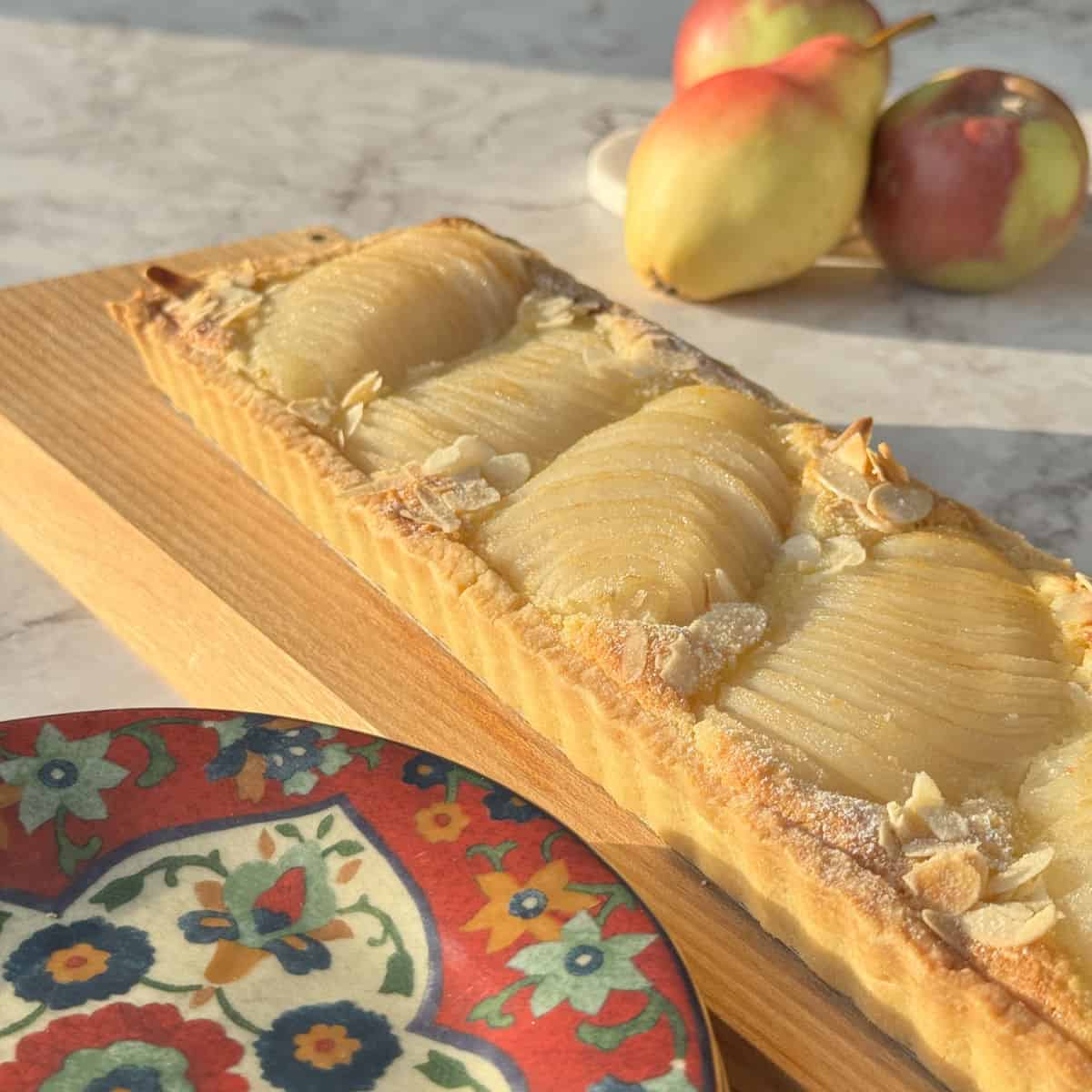 Pear tart with fresh pears in the background.