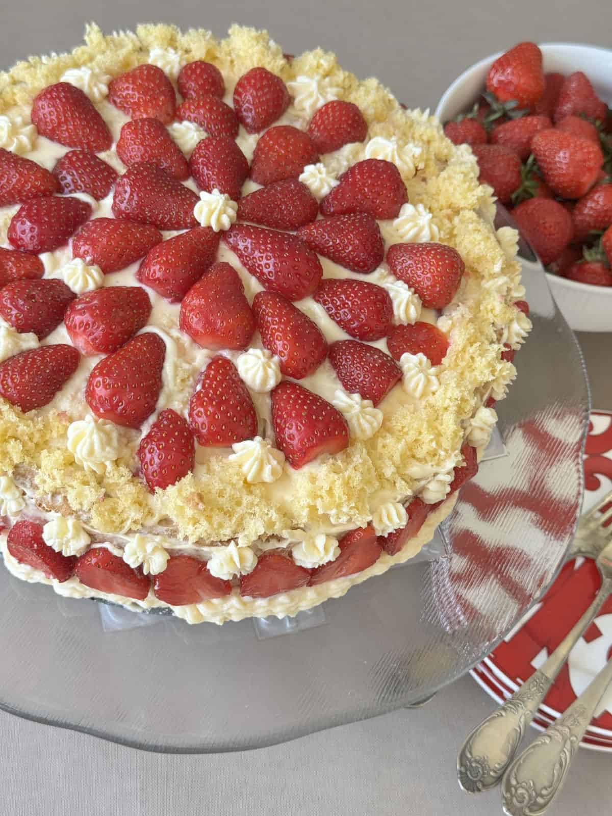 Strawberry cake with red plates and bowl of strawberries.