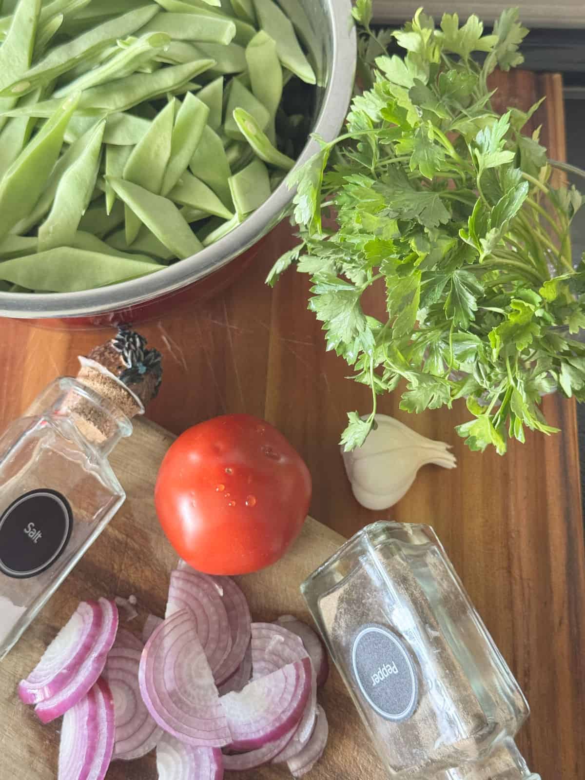 A close-up of fresh ingredients used in Green beans including Beans,, onion, garlic, tomato and parsley.
