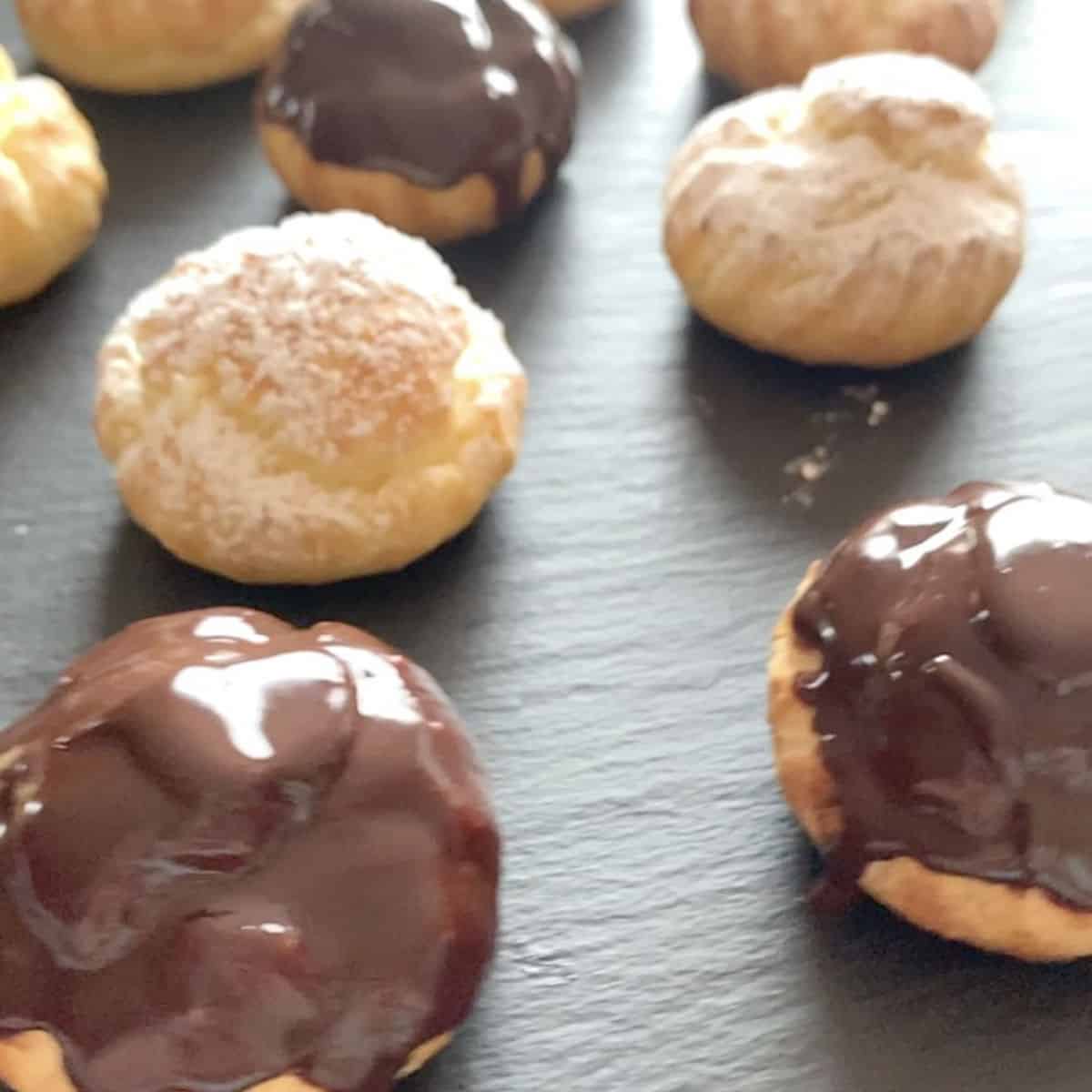 Profiteroles covers with powdered sugar and chocolate glaze on a slate.