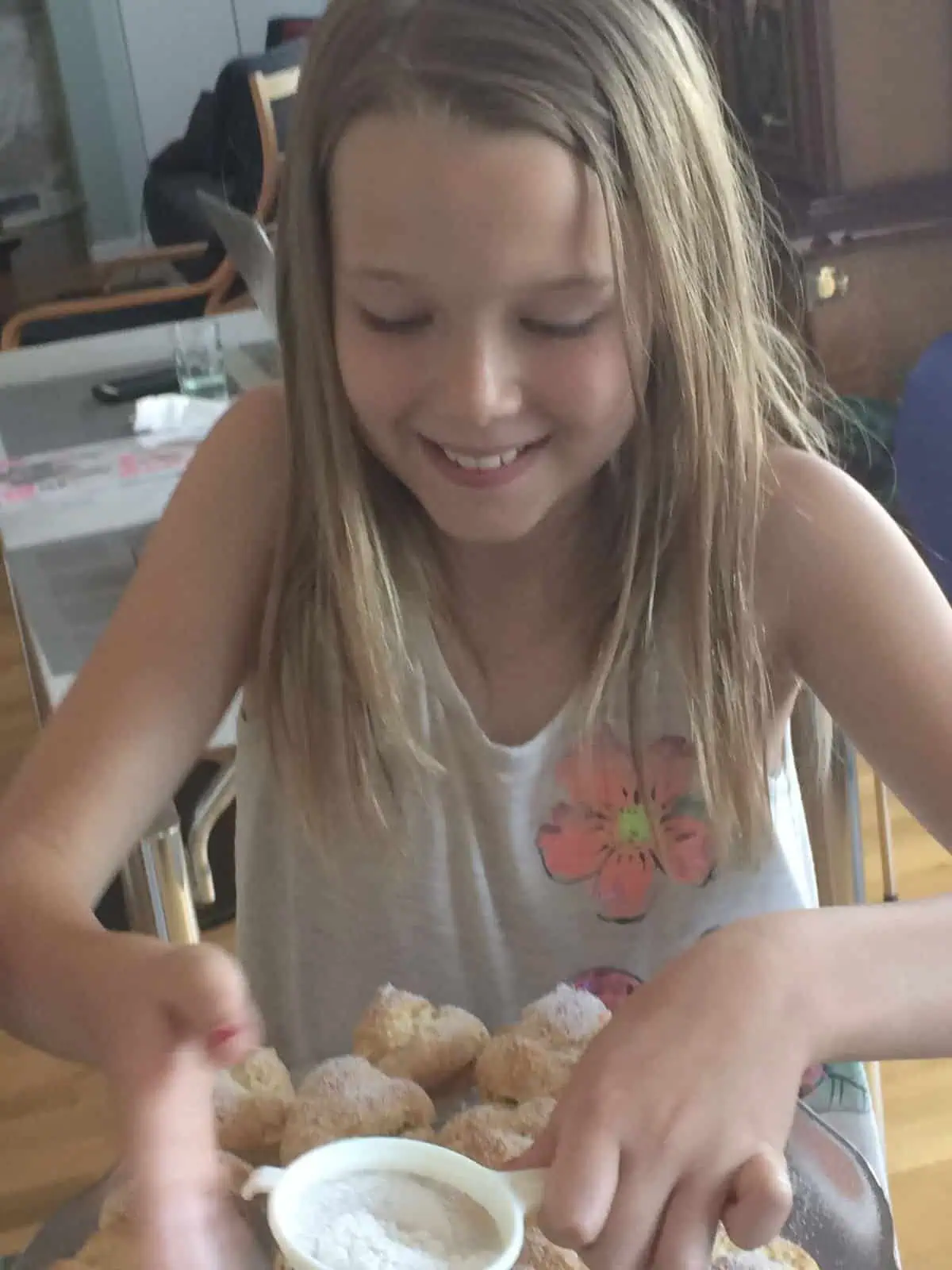 A girl sifting powdered sugar on cream puffs.