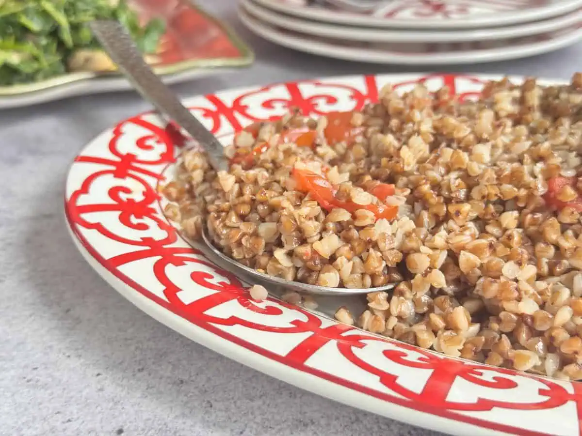 Buckwheat pilaf on a red plate with a spoon.