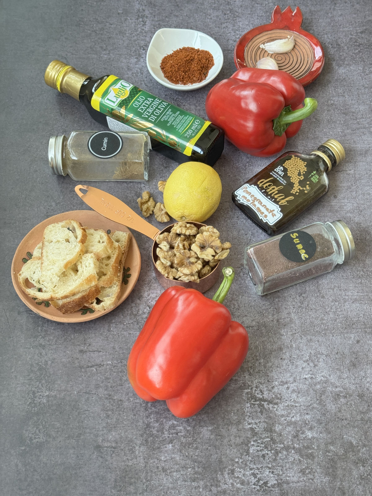 Muhammara ingredients grouped together: red bell peppers, walnuts, a bottle of pomegranate molasses, and spices in small bowls.