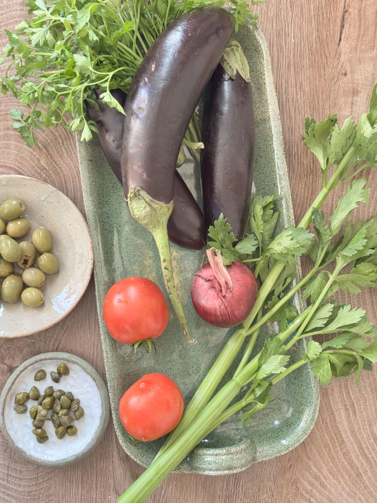 Ingredients for Sicilian caponata recipe — eggplant, tomatoes, celery, onion, olives, and capers arranged on a counter.