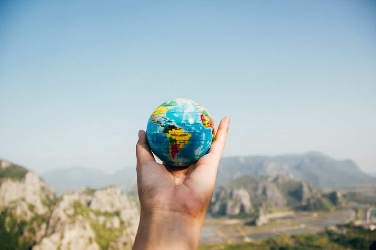 who-we-are-02 Hand holding a globe against a mountain background symbolizing travel and exploration.