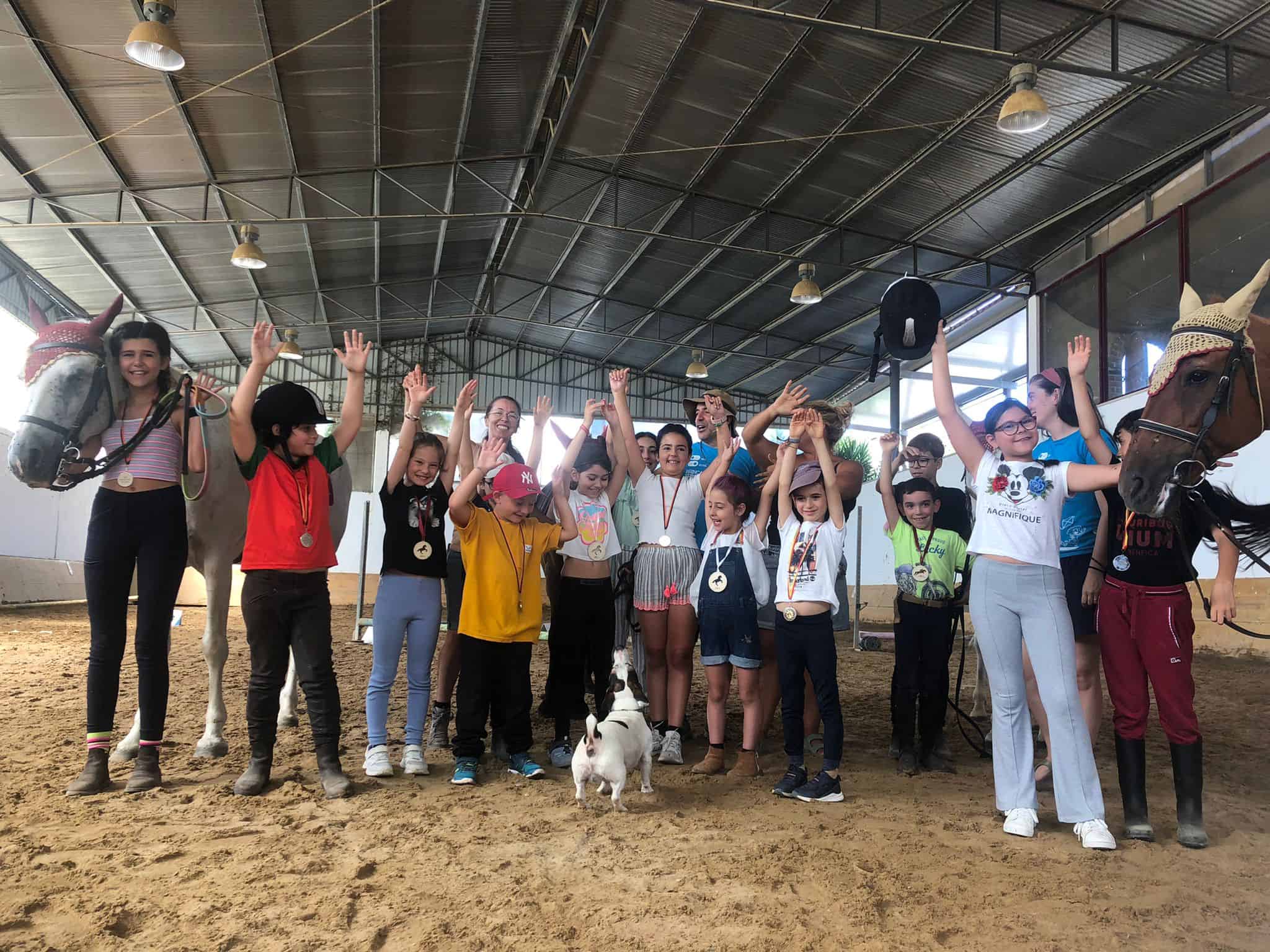 Group of children and adults celebrating with horses in an indoor riding arena.