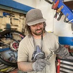 1. Man in workshop repairing bike, wearing gloves, with bike tools and bike parts in background.