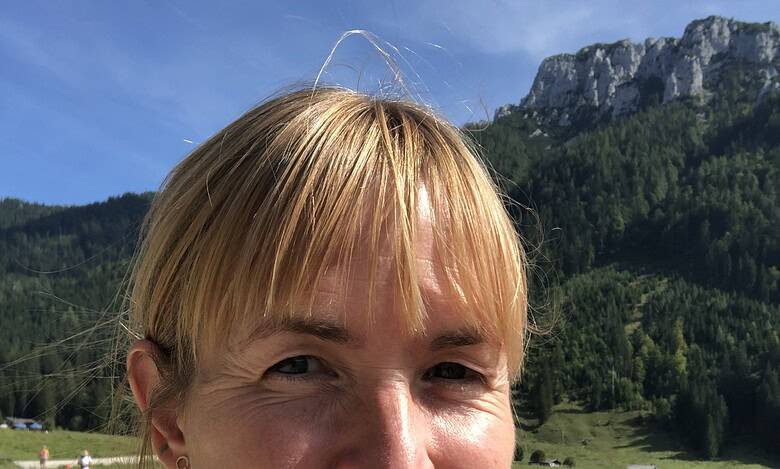 Bright woman hiking outdoors with green mountains and blue sky in the background, enjoying nature.