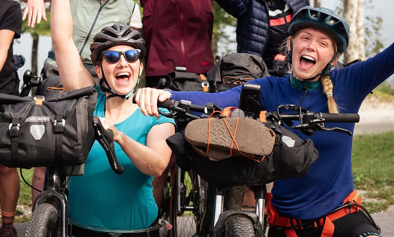 Exciting group of women mountain biking outdoors with helmets and gear in a forest setting.