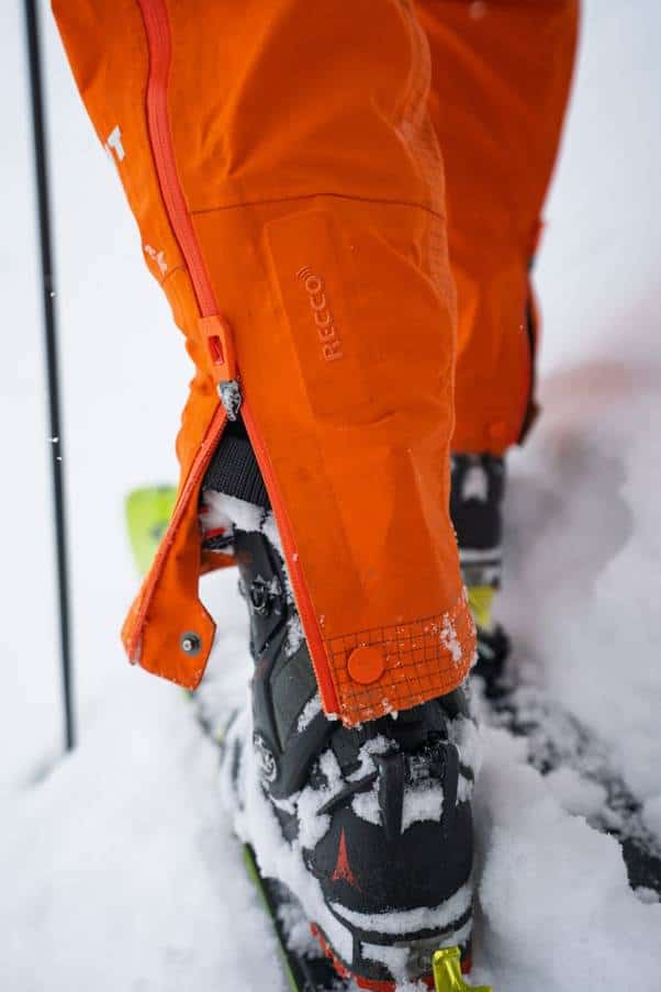 Bright orange waterproof winter jacket with snow-covered ski boots on snow-covered ground. Outdoor outdoor equipment, durable apparel.